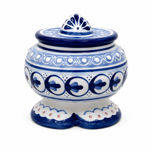 A traditional hand-painted ceramic jar with a lid, featuring a white base decorated with deep cobalt blue patterns, including floral motifs, scalloped borders, and a fan-shaped finial on top, set against a plain white background.