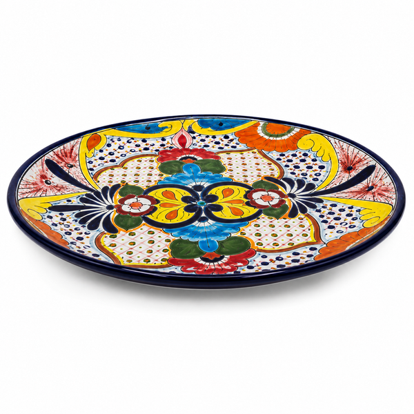 An oval ceramic plate with a vibrant, hand-painted Mexican Talavera style design featuring a central floral motif in yellow, blue, green, red, and orange on a white background with black dotted patterns.